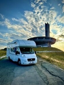 Camper Adria in sosta panoramica davanti al monumento Buzludzha in Bulgaria, con cielo al tramonto