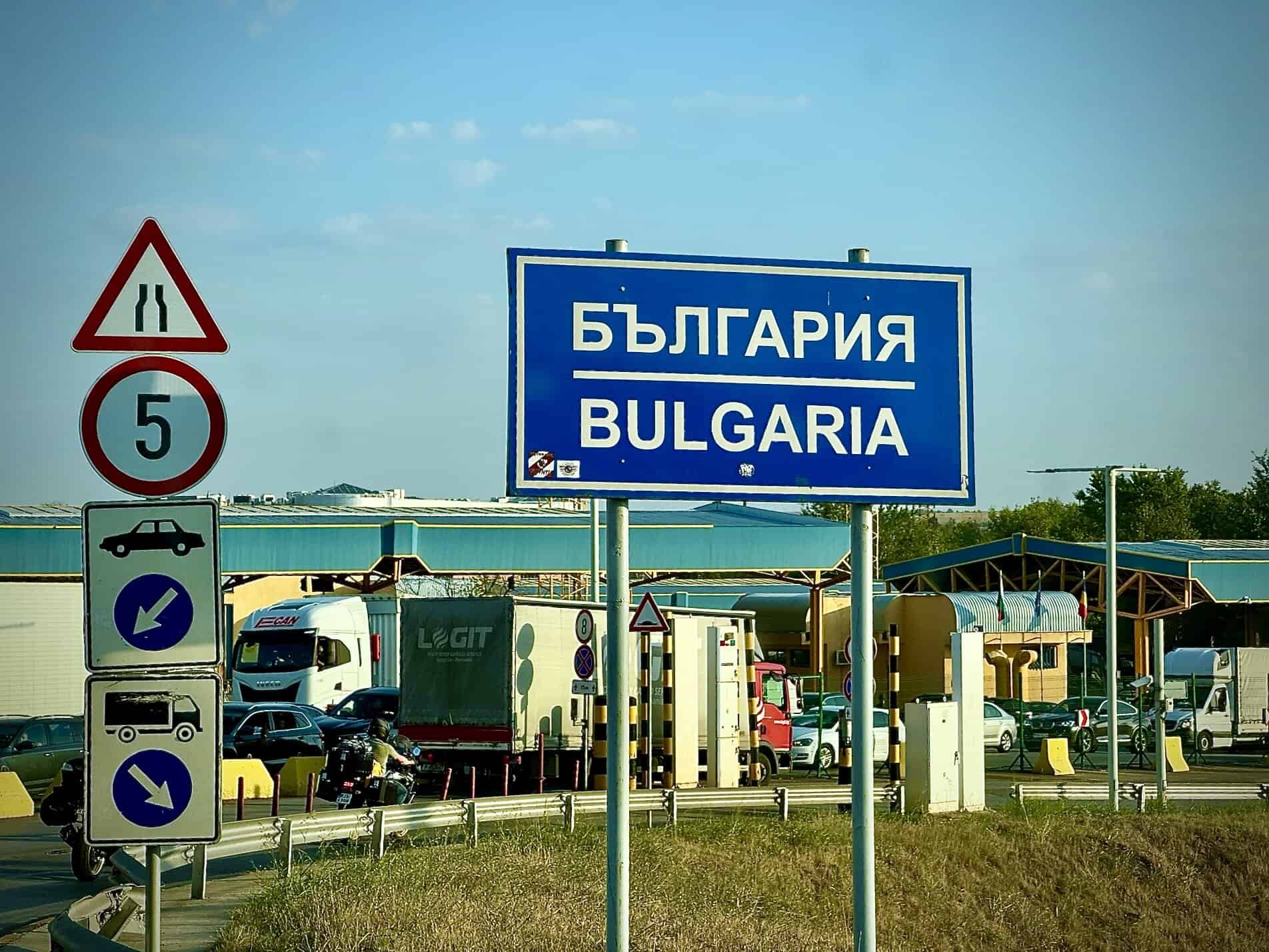 Cartello di confine Bulgaria con scritta in cirillico e traffico di auto e camion al valico di frontiera