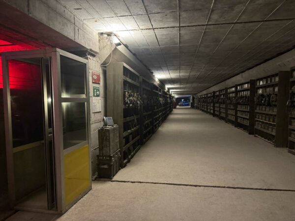 Lunga galleria in cemento del bunker antiatomico con scaffalature metalliche per lo stoccaggio.