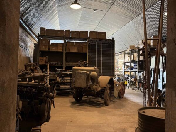Magazzino con casse militari, fusti di metallo e un carrello logistico d'epoca all'interno del bunker.