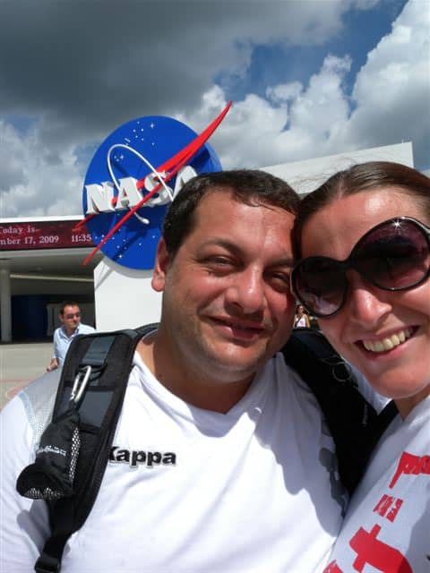 Due persone sorridenti davanti al logo NASA in un giorno soleggiato.