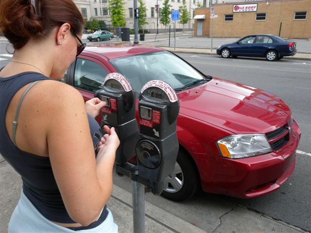 Donna utilizza parchimetro vicino a una vettura rossa in città.