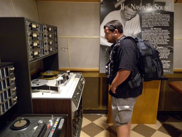 Studente in sala di registrazione con apparecchiature audio professionali.