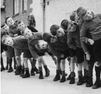 Gruppo di bambini in fila davanti a una scuola, sorridenti e felici.