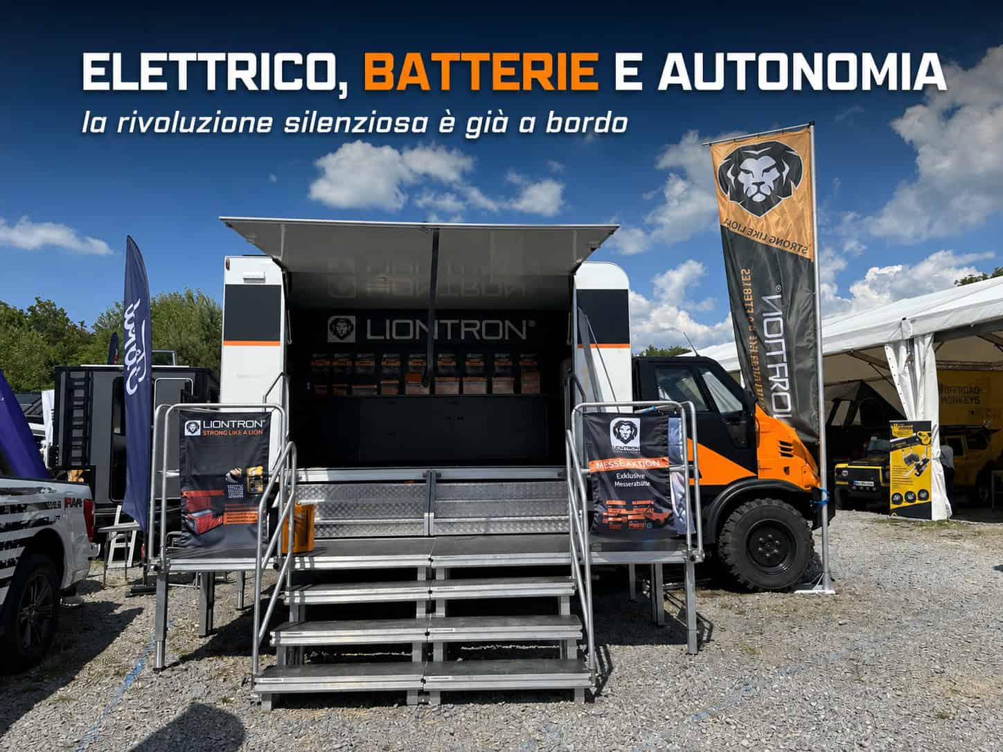 Il truck-palco dello stand Liontron ad Abenteuer & Allrad con batterie LiFePO4 esposte, bandiere del brand e camion Tekne arancione