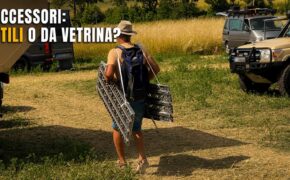 Visitatore di spalle trasporta due piastre da sabbia in alluminio appena acquistate verso il proprio mezzo, tra camper e fuoristrada