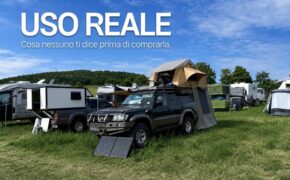 Fuoristrada in una camp area con tenda da tetto morbida aperta, accessorio veranda montato e pannello solare appoggiato al paraurti; titolo Uso reale nel cielo.