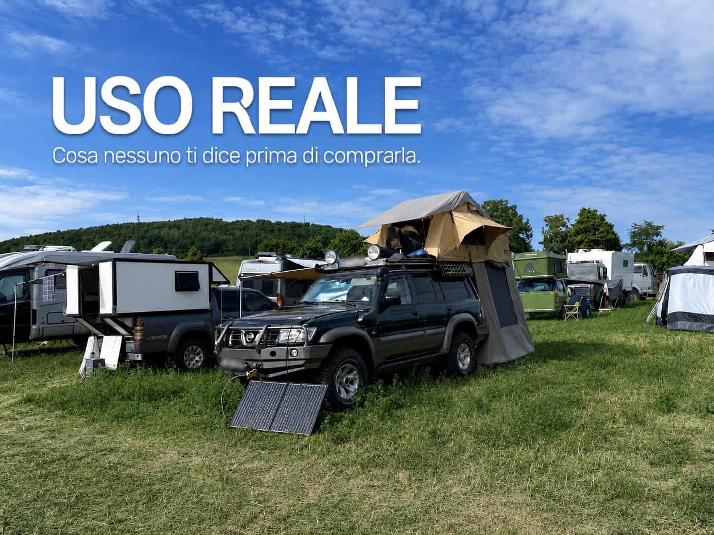 Fuoristrada in una camp area con tenda da tetto morbida aperta, accessorio veranda montato e pannello solare appoggiato al paraurti; titolo Uso reale nel cielo.