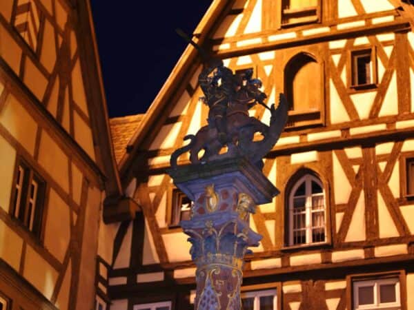 La statua di San Giorgio e il drago su una fontana, tra case a graticcio illuminate di notte, Rothenburg ob der Tauber