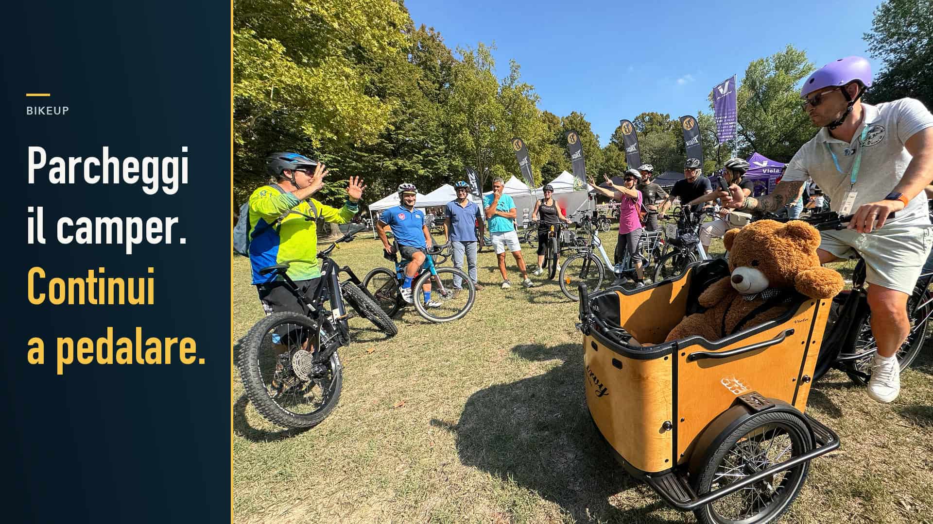 Prova di biciclette a BikeUP al Parco della Cittadella, con cargo bike in primo piano. Testo: Parcheggi il camper. Continui a pedalare.