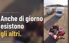 Gruppo di camperisti in cerchio nel parcheggio del Salone del Camper 2026 a Parma, ripreso dall&rsquo;alto con i camper dietro. Testo: Anche di giorno esistono gli altri.