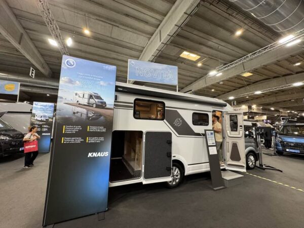 Knaus SKY TI VW visto di fianco allo stand Knaus, con il pannello della scheda e il garage aperto