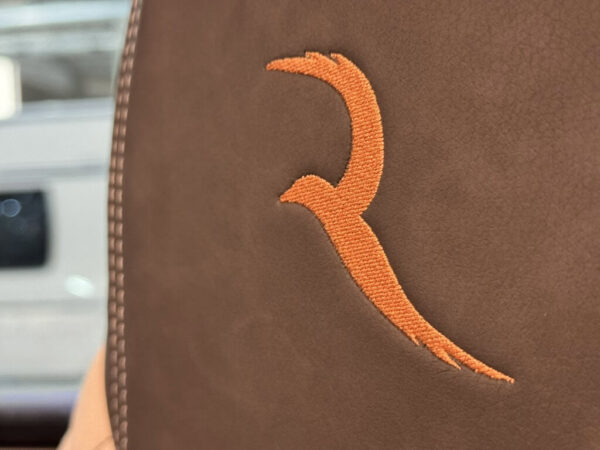 Logo Robeta ricamato in arancione sulla pelle marrone del sedile