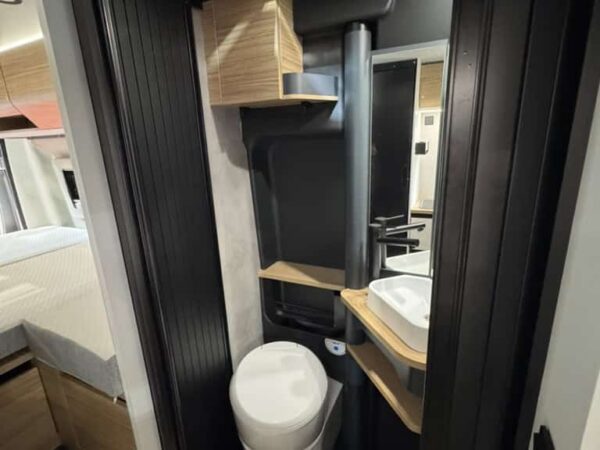 Bagno dell’Atlantis Carbon 4x4 con pareti scure, lavabo, specchio, oblò e wc, visto dalla porta