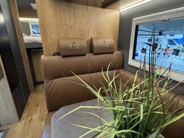 Dinette dell’Atlantis Carbon 4x4 con i sedili in pelle marrone, i poggiatesta con il logo, il tavolo grigio, la TV e i pensili in legno chiaro