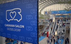 Ingresso del Caravan Salon D&uuml;sseldorf 2026 con il banner della fiera e i visitatori sulle scale mobili