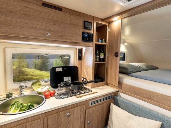 La cucina della Box 200 Super Light: fornello a gas a due fuochi con coperchio in vetro, lavello rotondo e pannello di controllo in alto; a destra il letto in alcova.