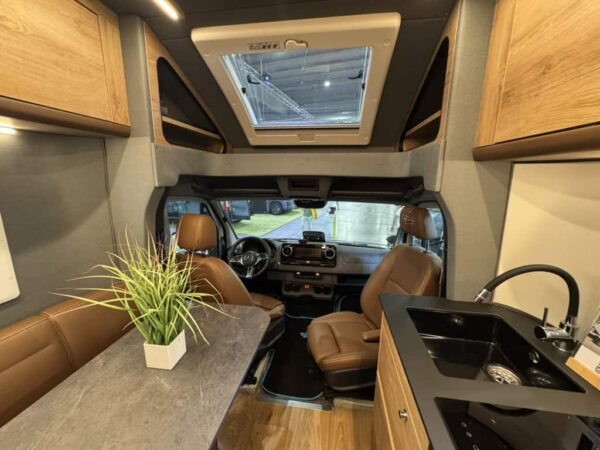 Interno dell’Atlantis Carbon 4x4 visto dalla dinette in pelle marrone verso la cabina dello Sprinter, con il lavello nero a sinistra e l’oblò sopra