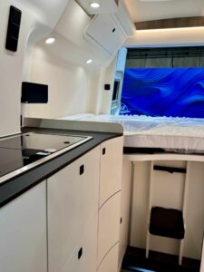 Cucina del Westfalia James Cook con piano cottura e, dietro, il letto posteriore