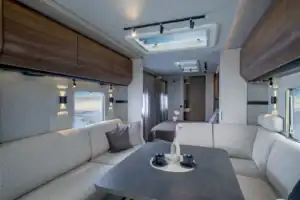 Interno della Knaus Nordwind 660 UDF: la dinette a U anteriore con l&rsquo;obl&ograve; sopra il tavolo e il letto fisso in fondo oltre la tenda