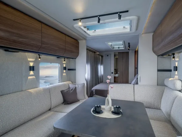 Interno della Knaus Nordwind 660 UDF: la dinette a U anteriore con l&rsquo;obl&ograve; sopra il tavolo e il letto fisso in fondo oltre la tenda